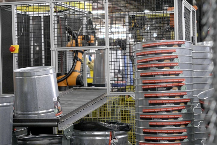 Metal pails entering safety cage with cobot inside